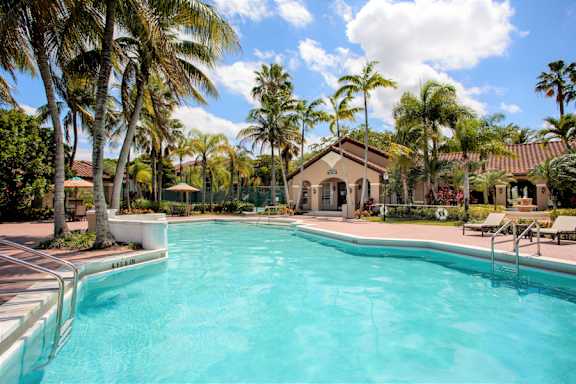 A swimming pool surrounded by palm trees and a building in the background.