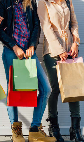 three women holding shopping bags and standing in front of a white wall