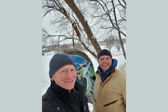 two people standing in the snow next to a tree