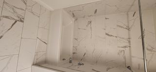 A white marble tiled shower with a white tub.