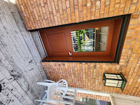 A window with a brown wooden door and a white chair on the wall.