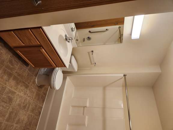 A white toilet with a wooden seat cover is in a bathroom with brown tiles.