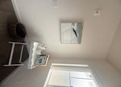 Thumbnail 9 of 14 - A mirror hangs on a wall above a shelf.
