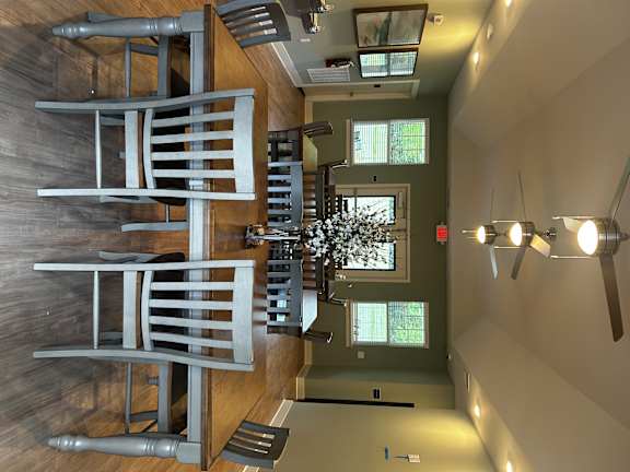 A large, modern chair is positioned in the center of a room with a wooden floor and a wall with a window.
