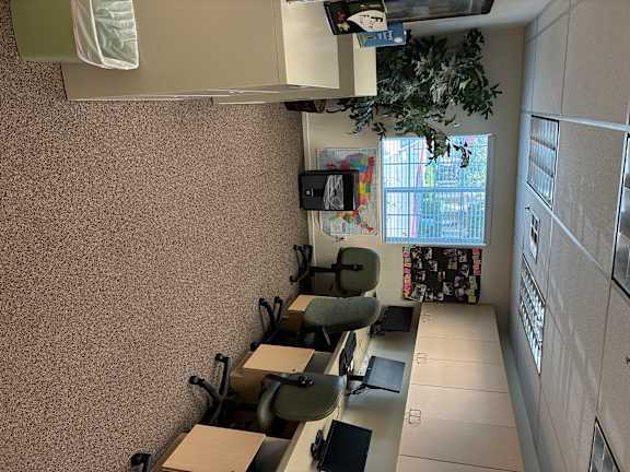A room with a desk, chairs, and a bulletin board.