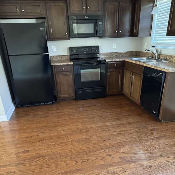 A black fridge in a kitchen with wooden cabinets and microwaves.