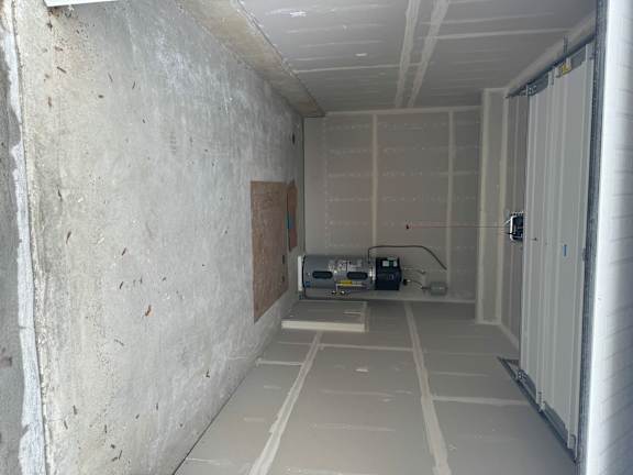A room with a white ceiling and walls, with a window on the left side.