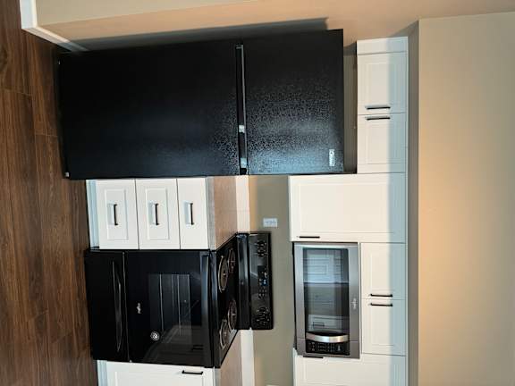 A black fridge in a kitchen with a white oven and microwave.