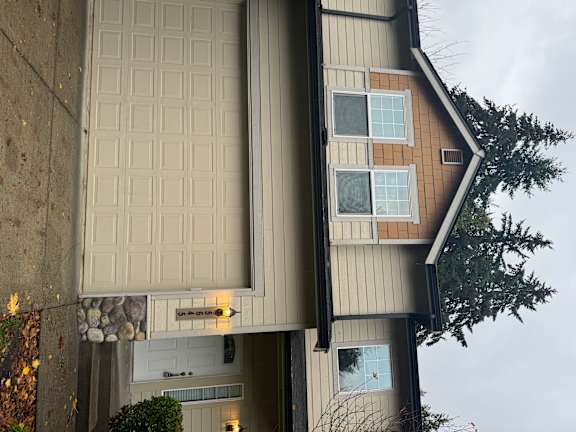 A house with a brown and beige exterior and a white garage door.