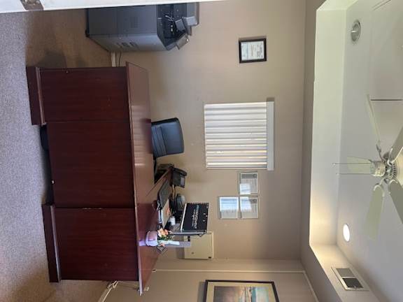 A room with a ceiling fan, a window with blinds, and a cabinet with a monitor on top.