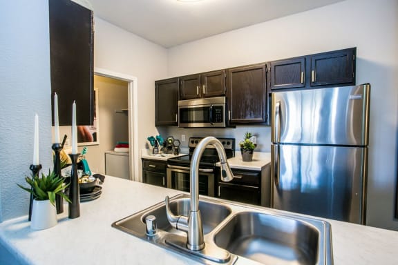 Kitchen with dark cabinets, stainless steel appliances, light counter tops and the laundry area to the back left.