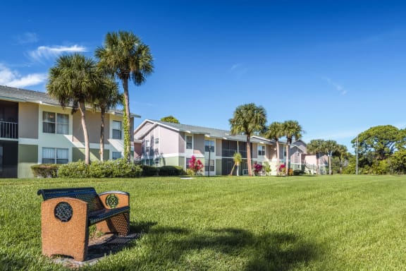Bench with lush grass and apartments in the background.