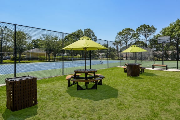 Grilling area with two picnic tables and a grill with the tennis court in the background.