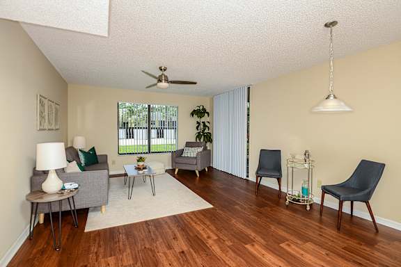Livingroom with area rug, couch, coffee table, arm chair, wood style flooring, handing lamp, two chairs and a small table.