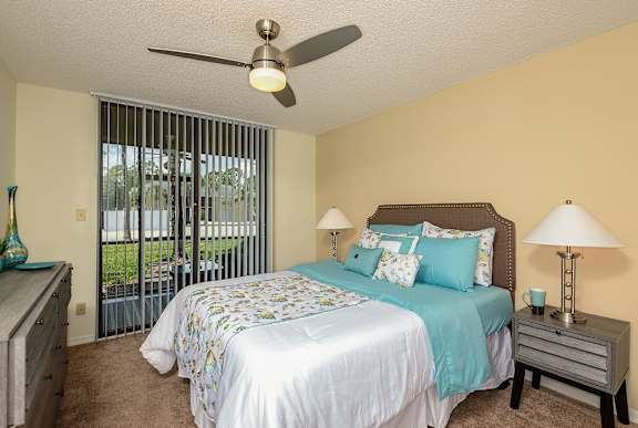 Bedroom with bed, two nightstands, two table lamps, ceiling fan, carpeting and sliding glass door to patio.