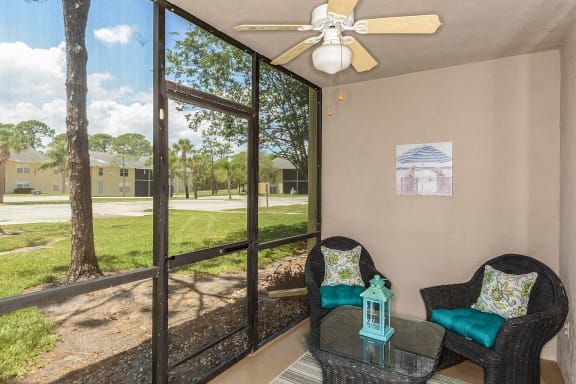 Screened in patio with door to outside, ceiling fan, patio chairs, table, area rug and wall art.