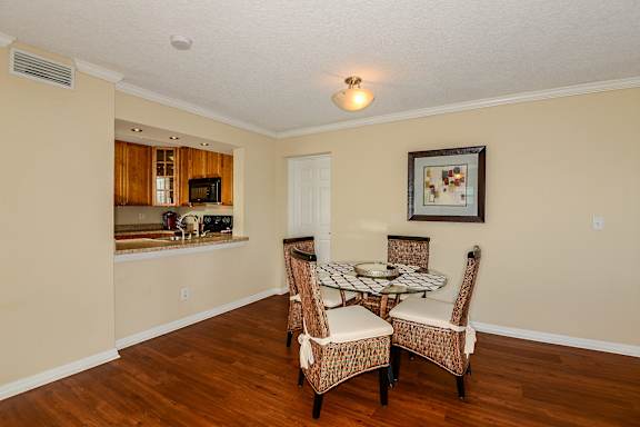 Dining area with glass top table, four chairs, wall art, wood like style flooring and a passthrough to the kitchen.