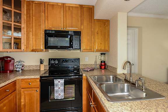 Wood style cabinets with stone like countertops, black appliances and stainless steel sink.