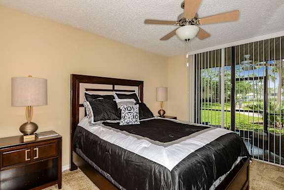 Bed with two night stands, two table lamps, ceiling fan and slider out to patio.