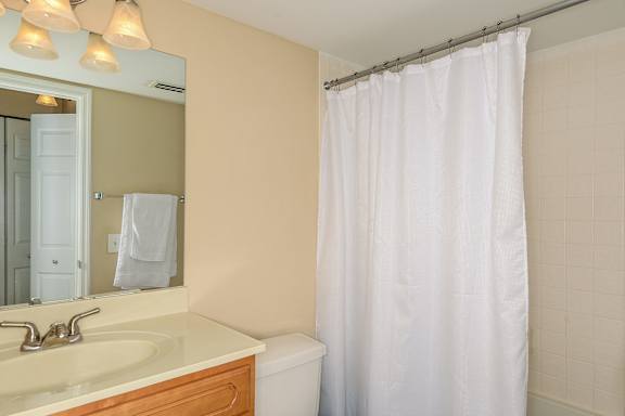 Bathroom with white toilet, wood style vanity, white counter top and silver fixtures.