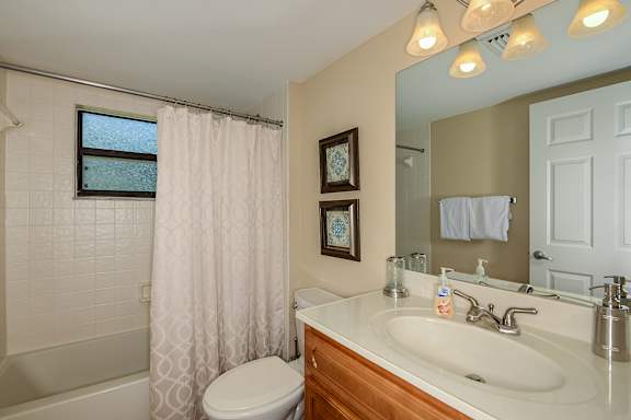 Bathroom with wood color vanity, white sink, white toilet, white shower/tub combo and