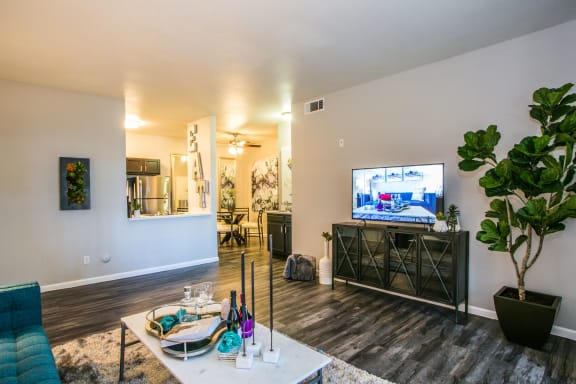 Living room with TV stand, large TV, wood flooring, area rug and entrance to the kitchen.