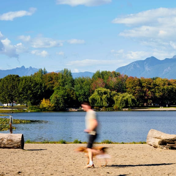 a man running with his dog on the beach near a lake