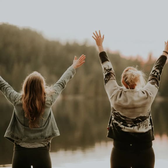 two women standing by a lake with their arms in the air