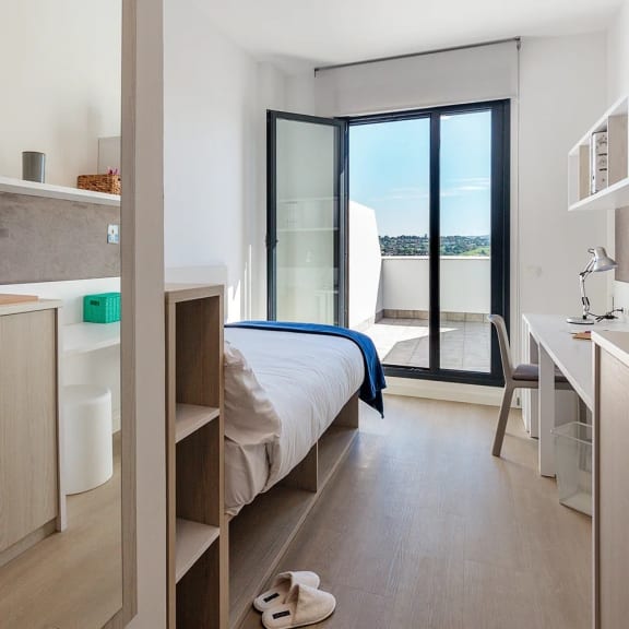 a bedroom with a bed and a desk and a balcony