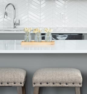 a kitchen with white quartz countertops and two stools with beige cushions