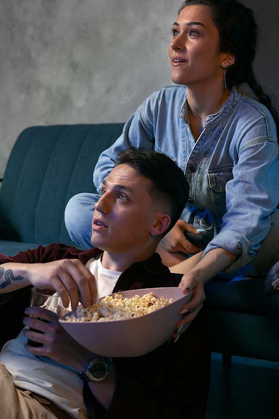 A man and woman sitting on a couch with a bowl of popcorn in front of them at Beton Apartments, Wembley, HA9 0SL