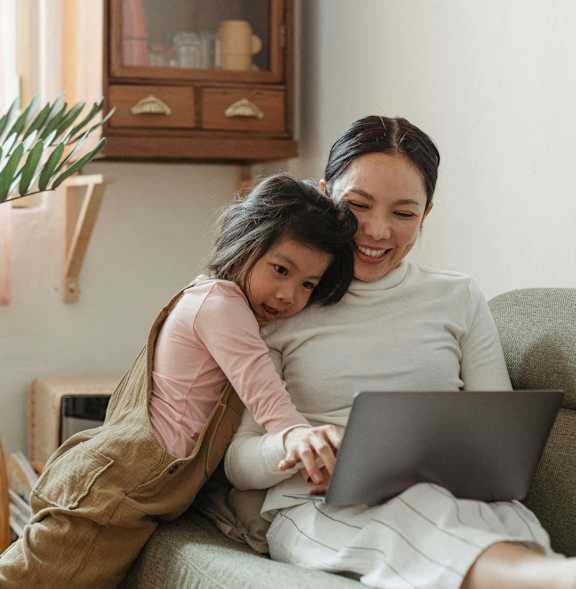 A woman and a child are sitting on a couch with a laptop.