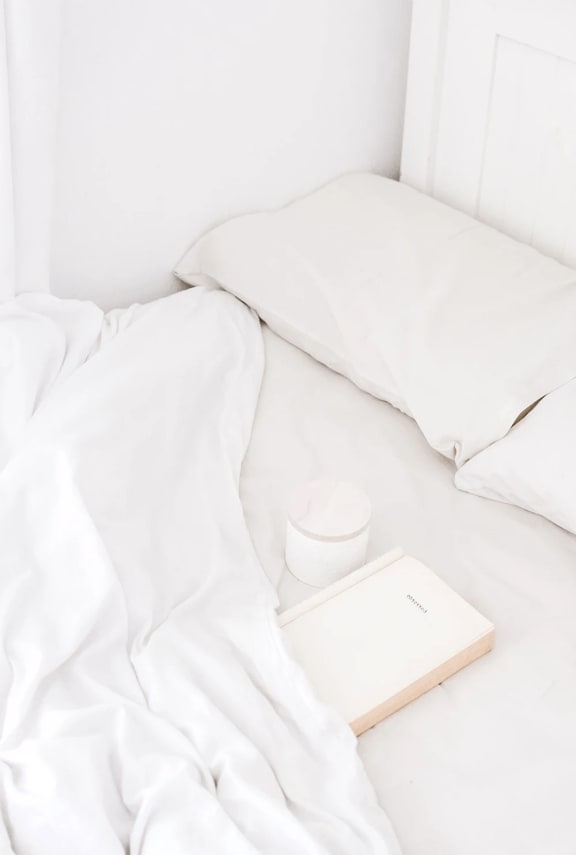 an unmade bed with white sheets and a book on top of it