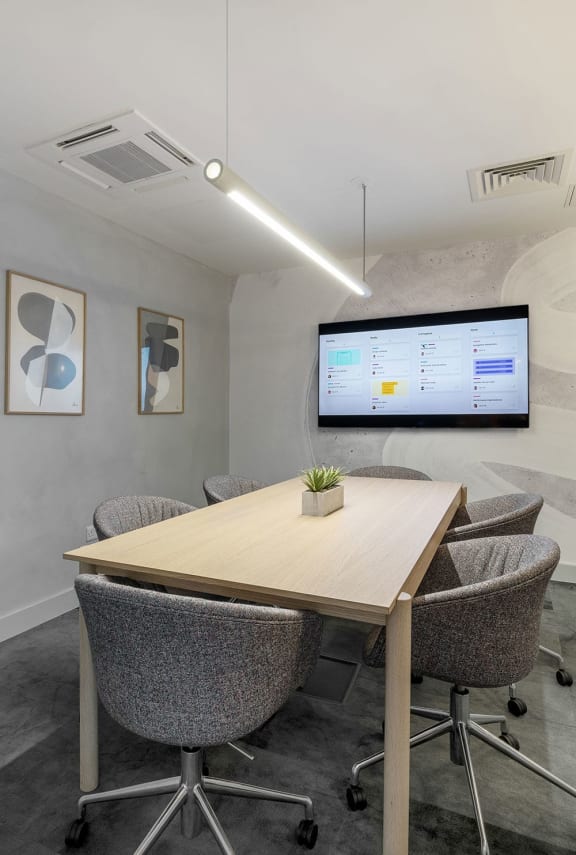 a meeting room with a table and chairs and a monitor on the wall