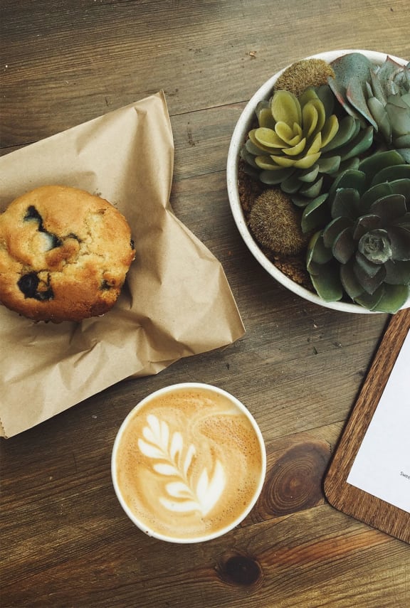 a cup of coffee and a muffin on a wooden table next to a plant