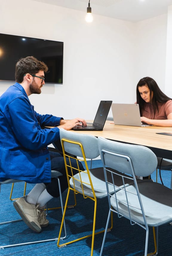 two people sitting at a table working on laptops