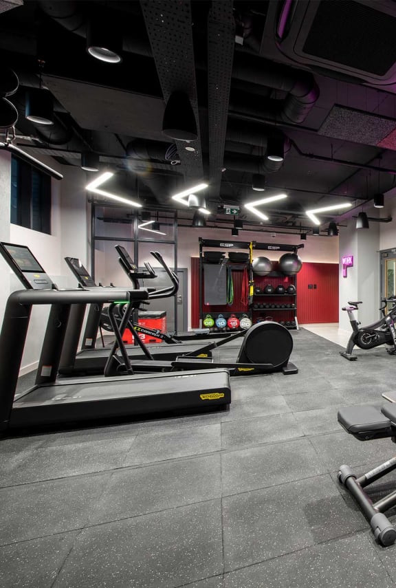 a gym with treadmills and other equipment in a gym space with red walls