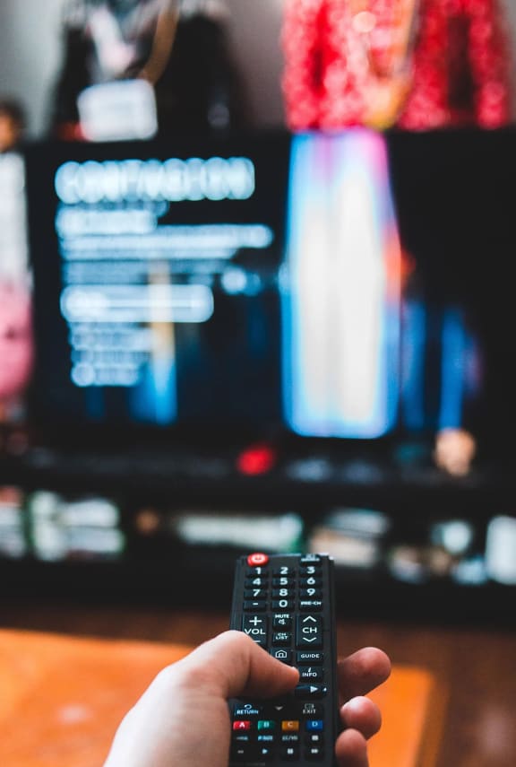 a hand holding a remote control in front of a tv