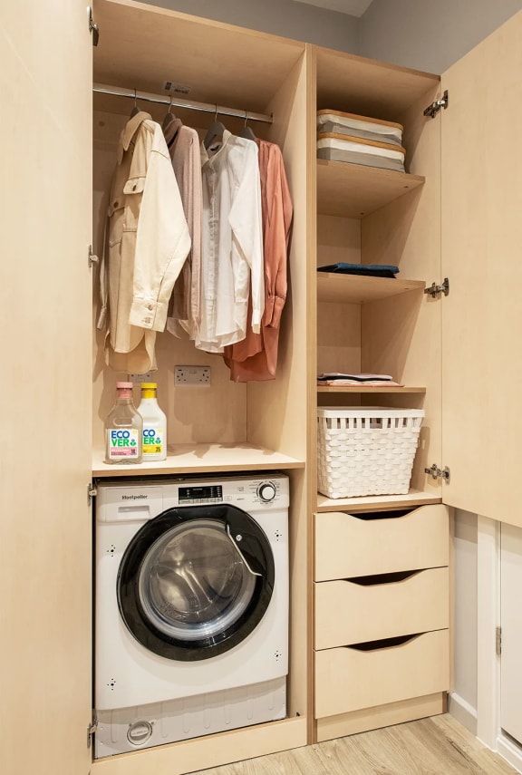 a small laundry room with a washing machine and a closet with clothes hanging