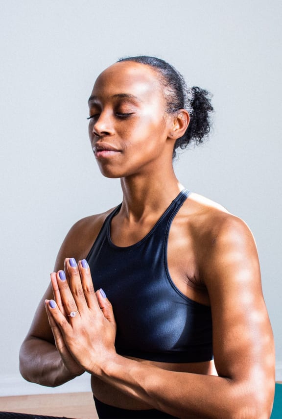 a woman in a black tank top praying with her hands on her chest