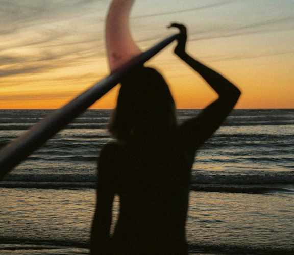 a woman holding a surfboard on the beach at sunset