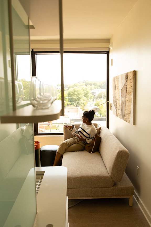 A woman is sitting on a couch in a room with a window. at Scout Living, powered by Placemakr Apartments, Atlanta, GA, 30308