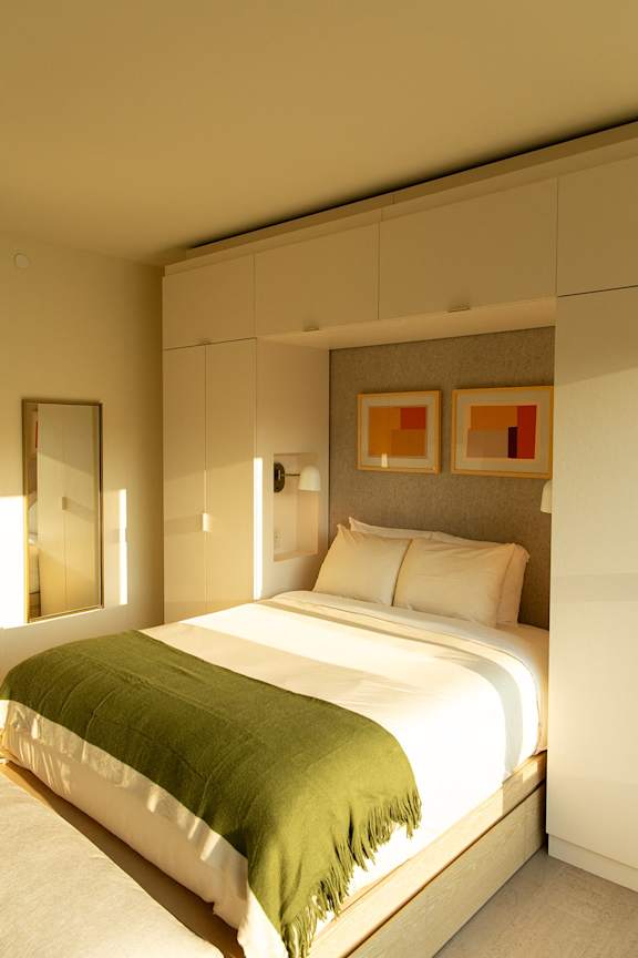 A bed with a green blanket is in a room with a mirror and two pictures on the wall. at Scout Living, powered by Placemakr Apartments, Atlanta, GA, 30308