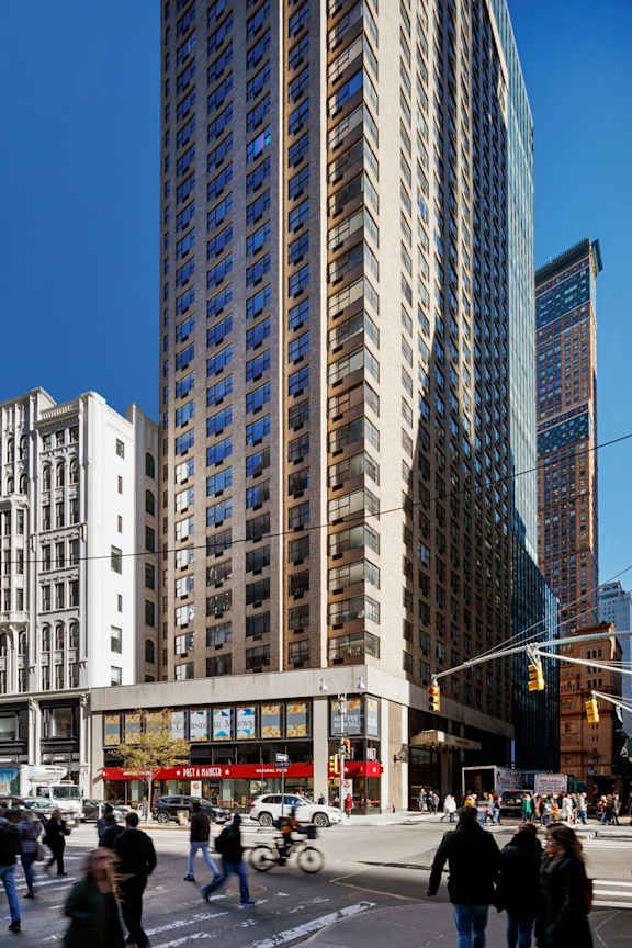 A tall building with many windows stands in the middle of a city street.