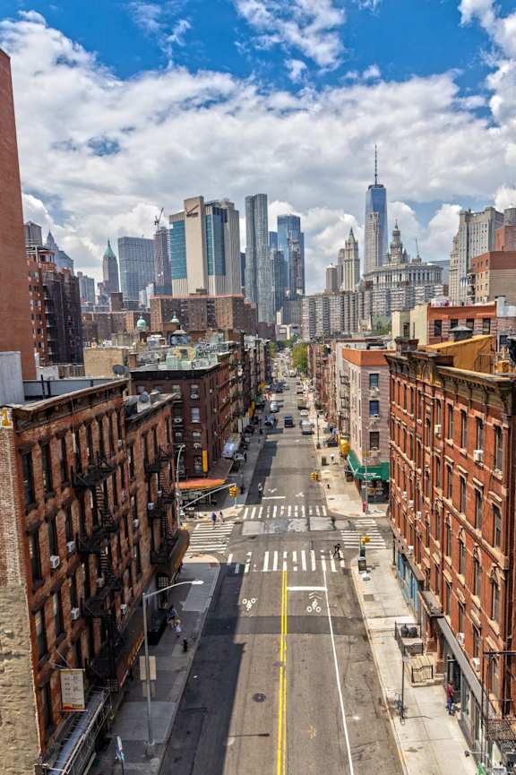A city street with buildings on both sides and a view of the city skyline in the distance.