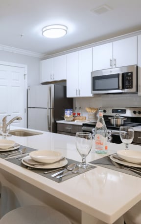 a kitchen with white cabinets and a white island with plates and glasses on it