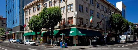 A street view of a city with cars parked on the side of the road and buildings with green awnings.