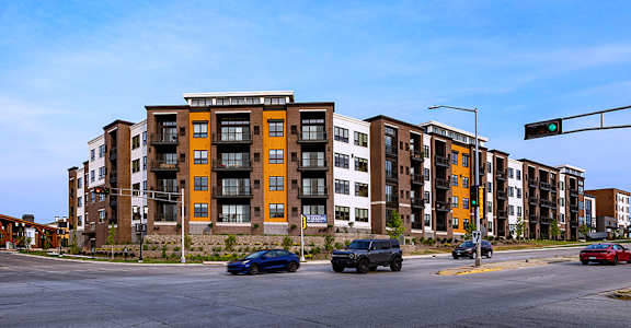 A street view of a multi-story apartment building with cars parked in front.