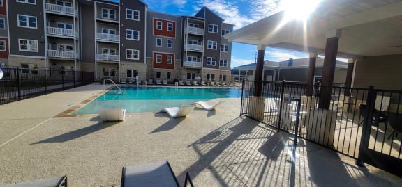 a swimming pool with lounge chairs and umbrellas in front of an apartment building