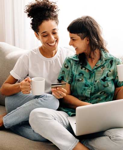 Two Women Sitting On a Couch Drinking Coffee While Using a Laptop at North Grove, Riverside, California